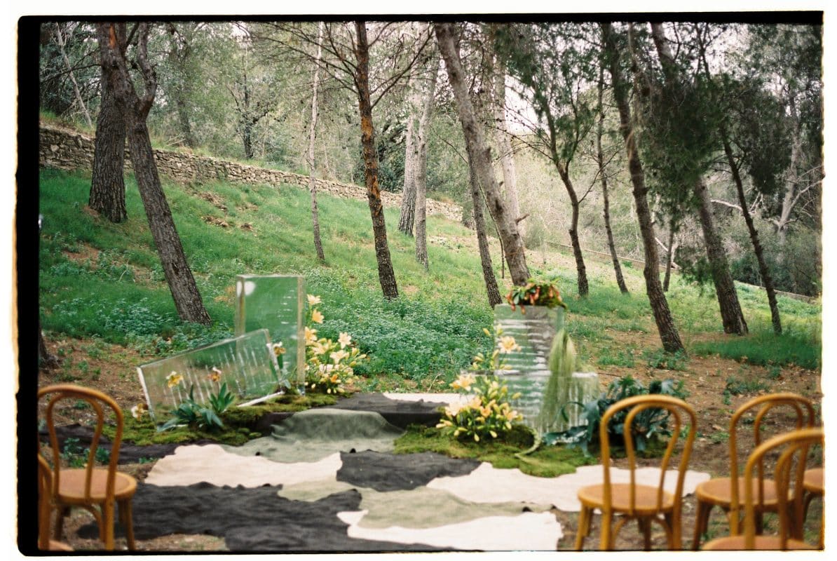 Pareja de novios en ceremonia civil al aire libre con sillas madera, flores frescas y decoración natural entre árboles.