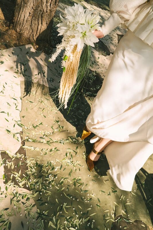 Pareja de novios en ceremonia civil al aire libre con sillas madera, flores frescas y decoración natural entre árboles.