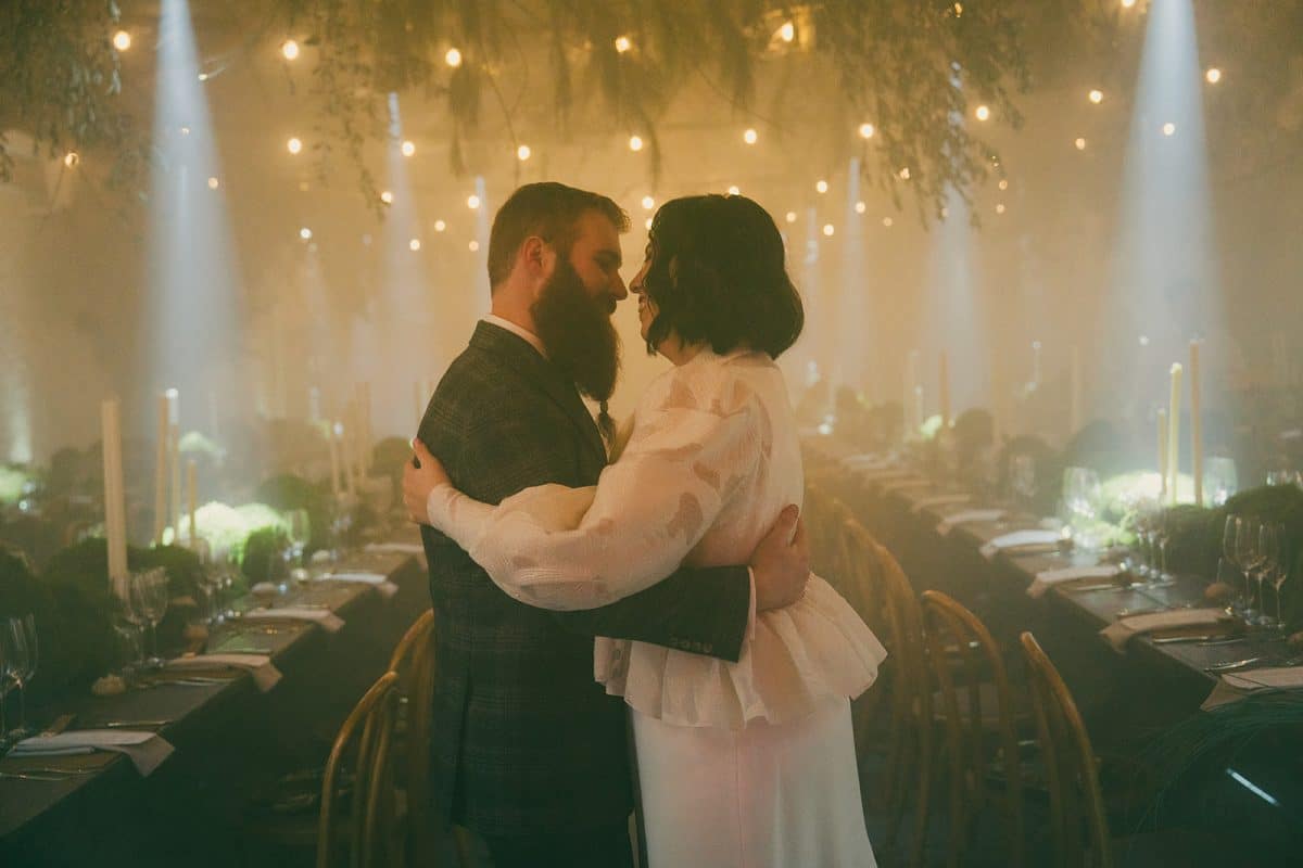 Mesa larga decorada con velas altas, musgo y cristalería en un ambiente estilo bosque encantado para cena de boda elegante.