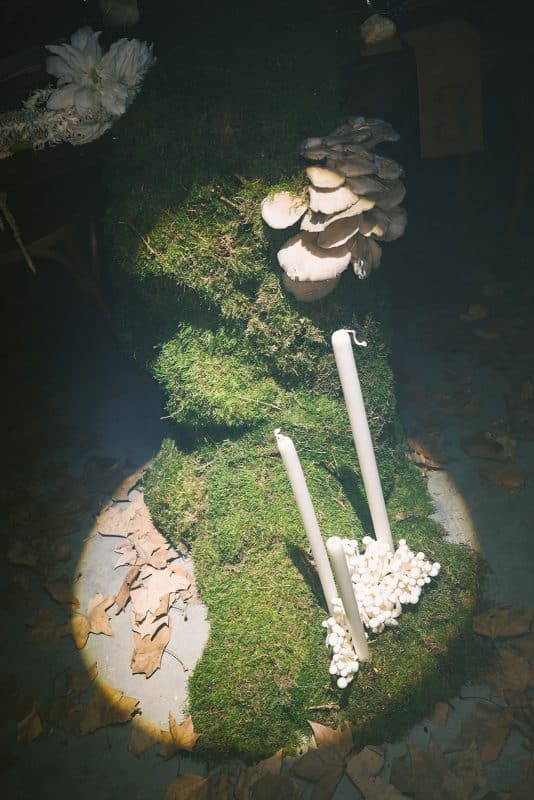 Mesa larga decorada con velas altas, musgo y cristalería en un ambiente estilo bosque encantado para cena de boda elegante.
