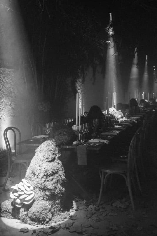 Mesa larga decorada con velas altas, musgo y cristalería en un ambiente estilo bosque encantado para cena de boda elegante.