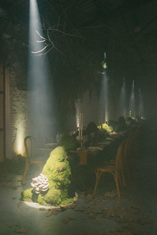 Mesa larga decorada con velas altas, musgo y cristalería en un ambiente estilo bosque encantado para cena de boda elegante.