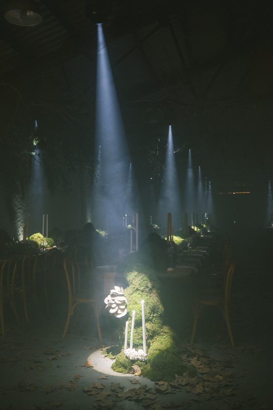 Mesa larga decorada con velas altas, musgo y cristalería en un ambiente estilo bosque encantado para cena de boda elegante.
