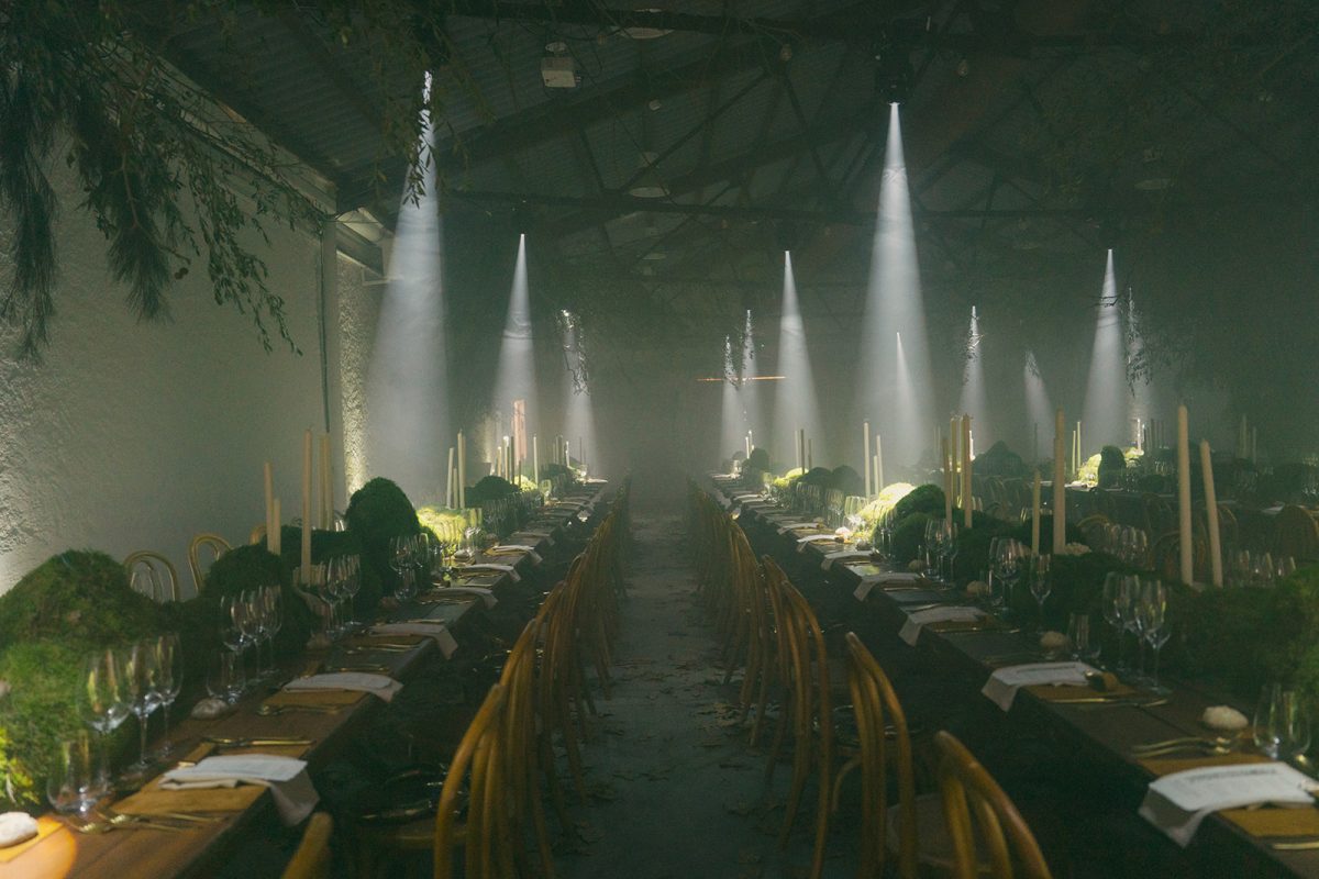 Mesa larga decorada con velas altas, musgo y cristalería en un ambiente estilo bosque encantado para cena de boda elegante.
