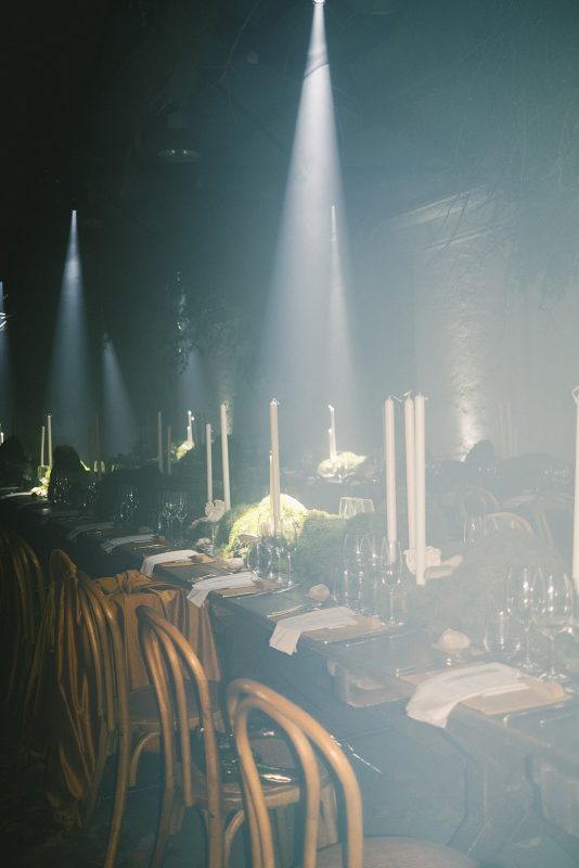 Mesa larga decorada con velas altas, musgo y cristalería en un ambiente estilo bosque encantado para cena de boda elegante.