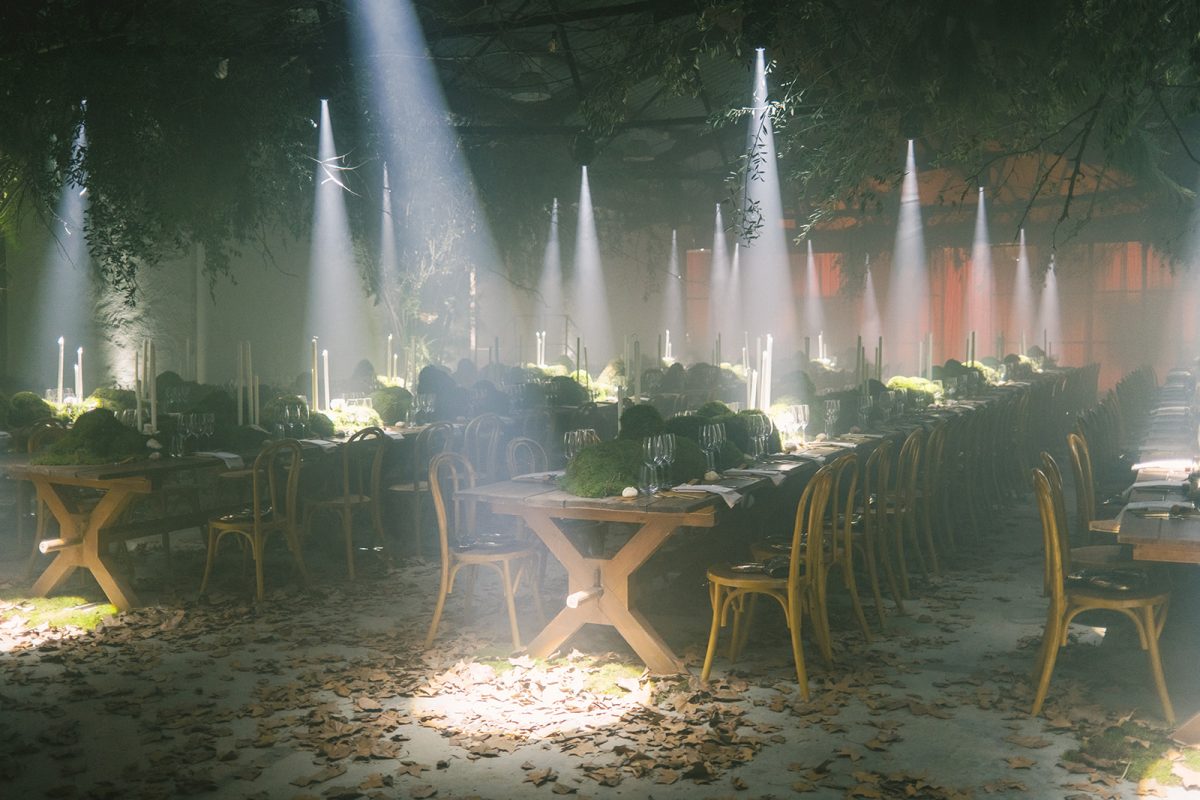 Mesa larga decorada con velas altas, musgo y cristalería en un ambiente estilo bosque encantado para cena de boda elegante.