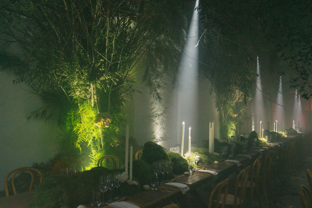 Mesa larga decorada con velas altas, musgo y cristalería en un ambiente estilo bosque encantado para cena de boda elegante.