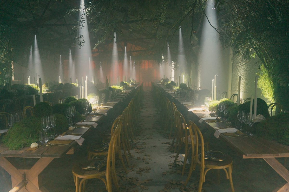 Mesa larga decorada con velas altas, musgo y cristalería en un ambiente estilo bosque encantado para cena de boda elegante.