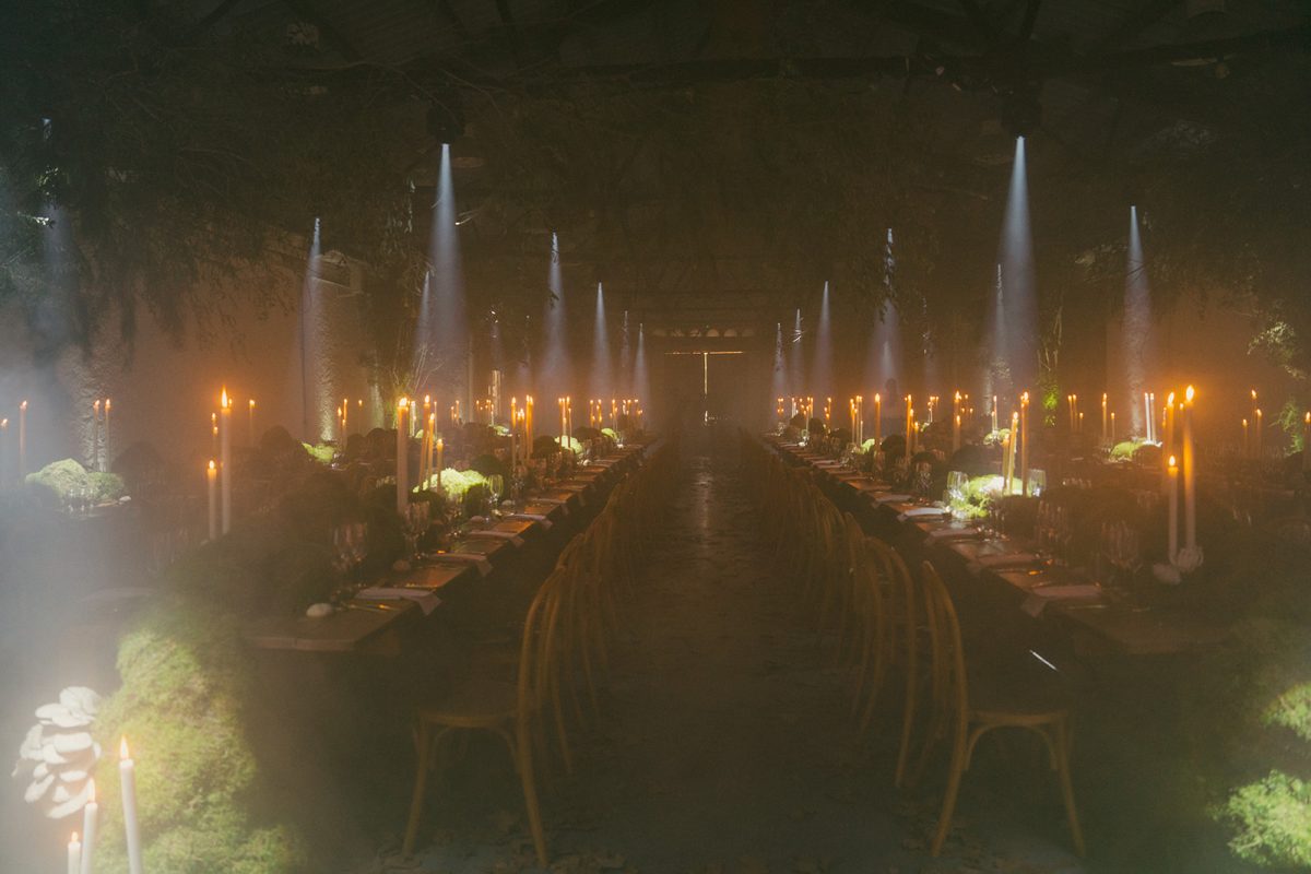 Mesa larga decorada con velas altas, musgo y cristalería en un ambiente estilo bosque encantado para cena de boda elegante.