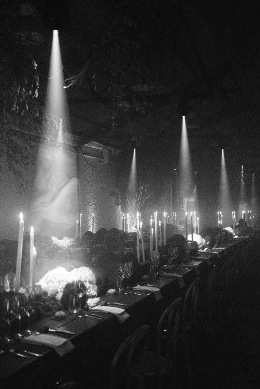 Mesa larga decorada con velas altas, musgo y cristalería en un ambiente estilo bosque encantado para cena de boda elegante.