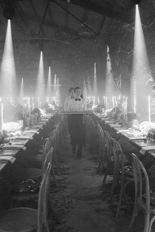 Mesa larga decorada con velas altas, musgo y cristalería en un ambiente estilo bosque encantado para cena de boda elegante.