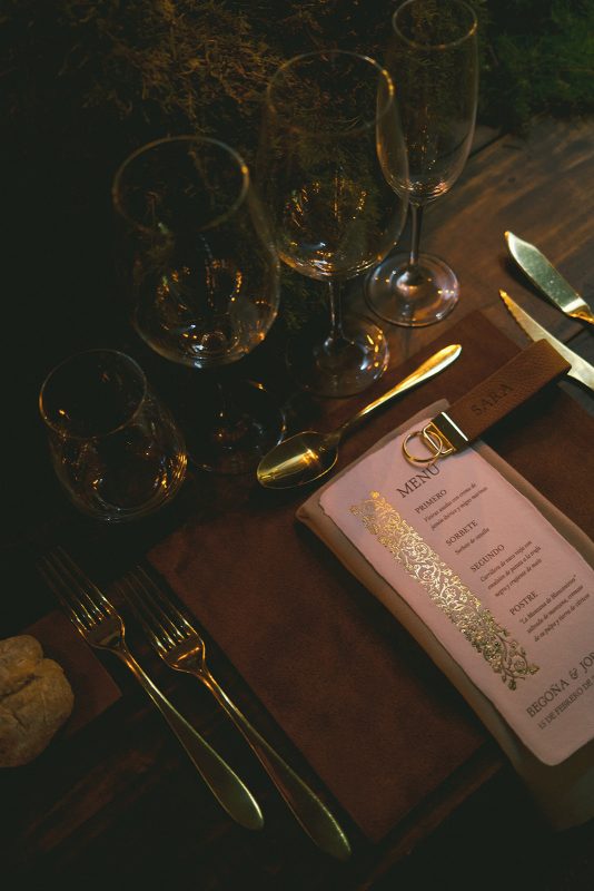 Mesa larga decorada con velas altas, musgo y cristalería en un ambiente estilo bosque encantado para cena de boda elegante.