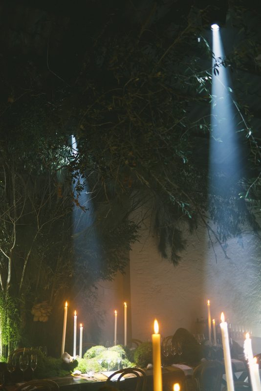 Mesa larga decorada con velas altas, musgo y cristalería en un ambiente estilo bosque encantado para cena de boda elegante.