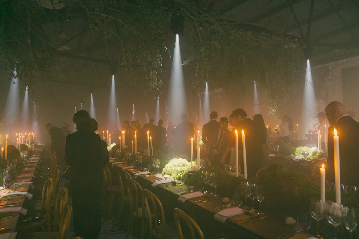 Mesa larga decorada con velas altas, musgo y cristalería en un ambiente estilo bosque encantado para cena de boda elegante.