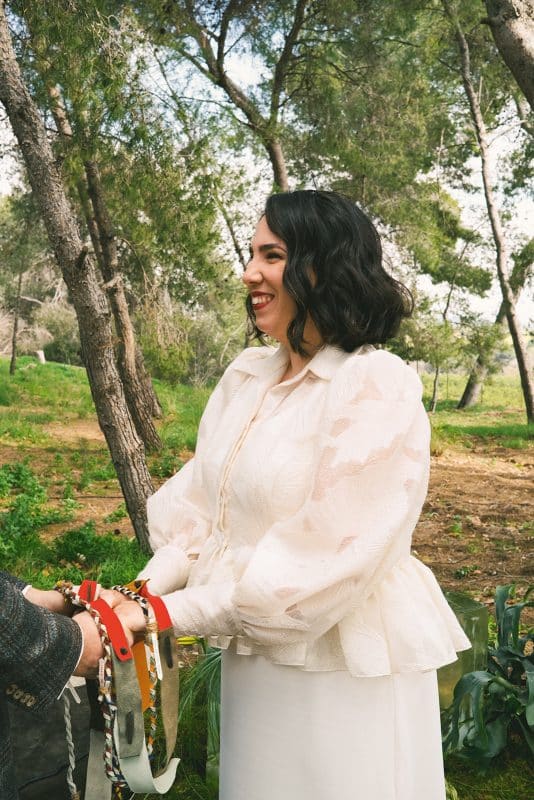 Pareja de novios en ceremonia civil al aire libre con sillas madera, flores frescas y decoración natural entre árboles.
