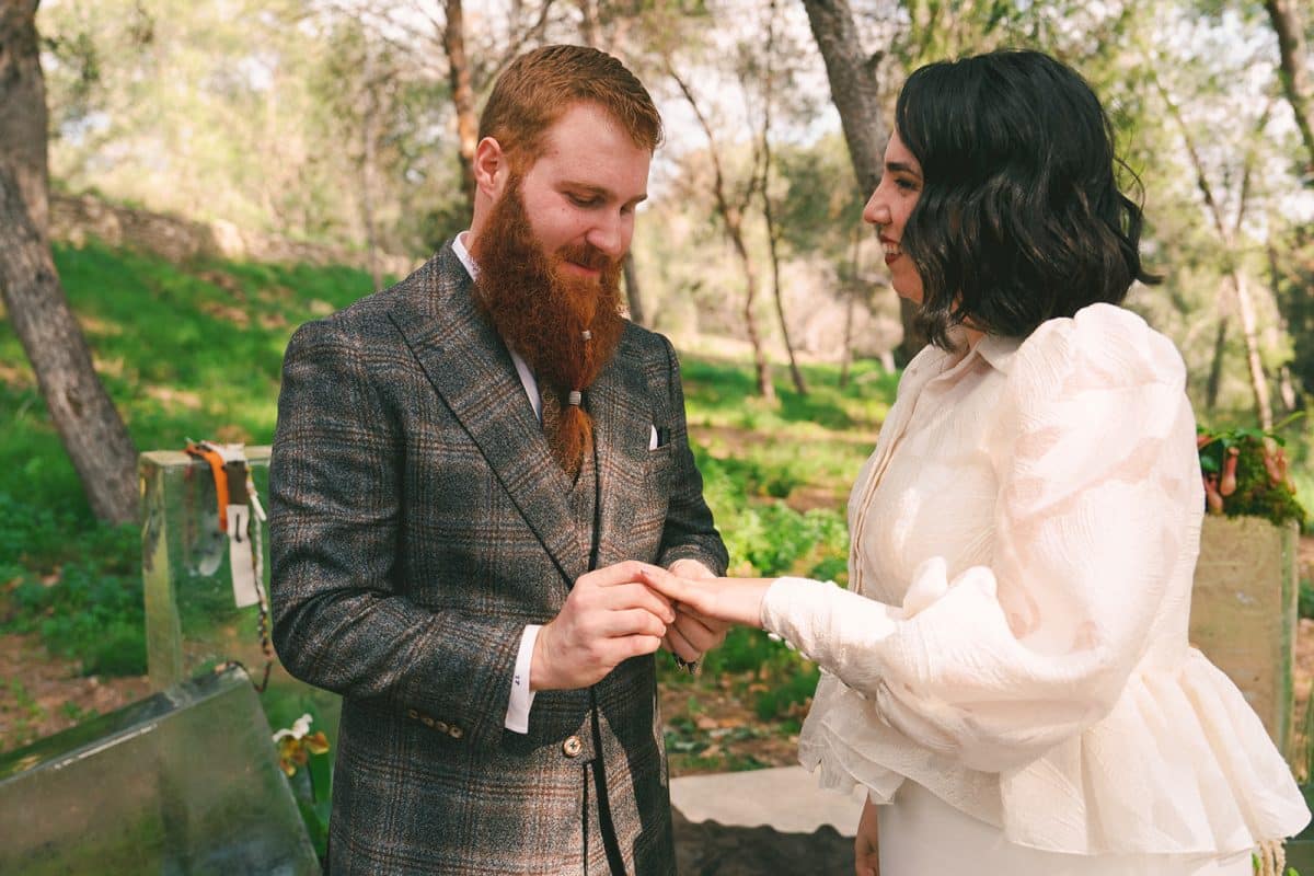 Pareja de novios en ceremonia civil al aire libre con sillas madera, flores frescas y decoración natural entre árboles.