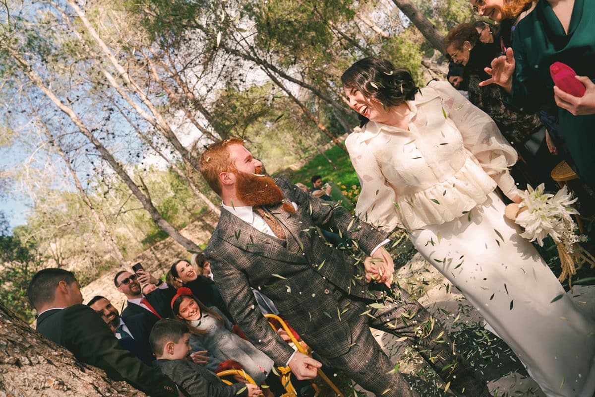 Pareja de novios en ceremonia civil al aire libre con sillas madera, flores frescas y decoración natural entre árboles.