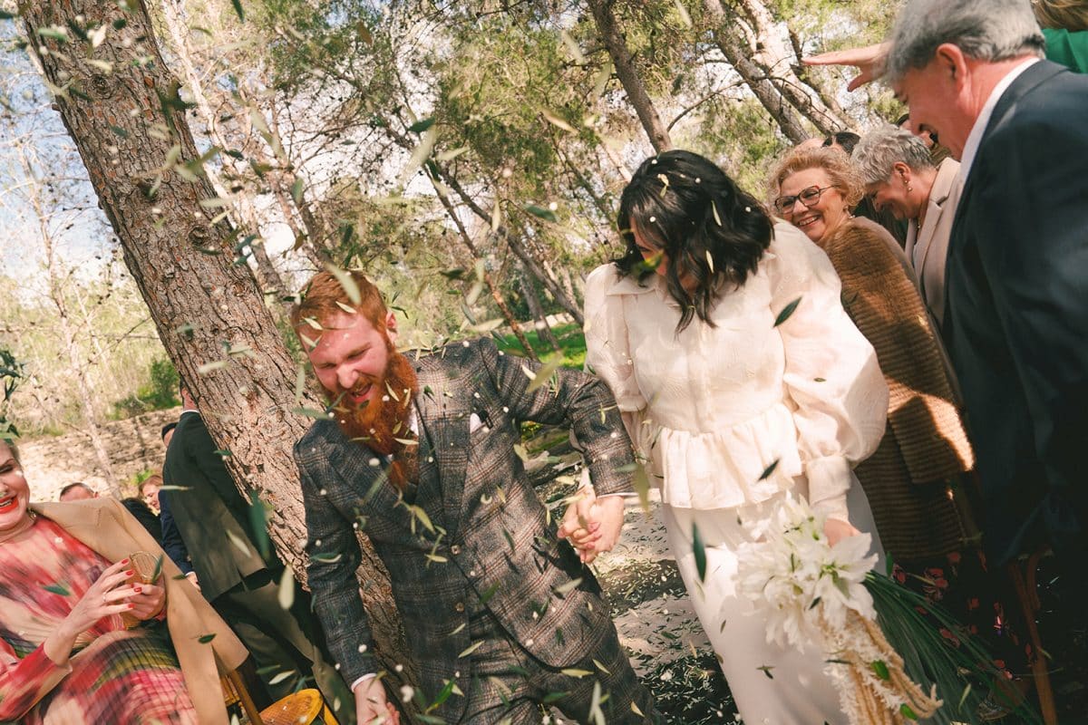 Pareja de novios en ceremonia civil al aire libre con sillas madera, flores frescas y decoración natural entre árboles.